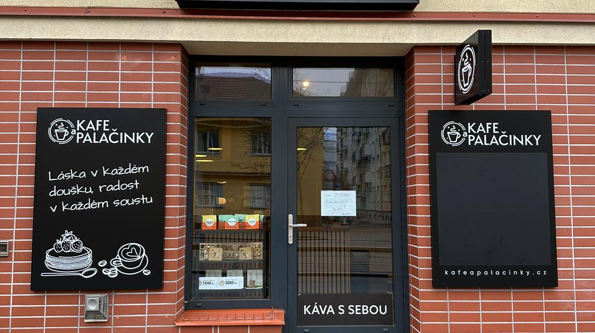 Průčelí provozovny — černá cedule s logem, křídové tabule s palačinkami a šálkem, výstrč se šálkem